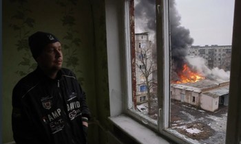 Một người đàn ông nhìn ra cửa sổ nơi đang có đám cháy sau vụ pháo kích ở Donetsk ngày 27/2. (Ảnh: AP)