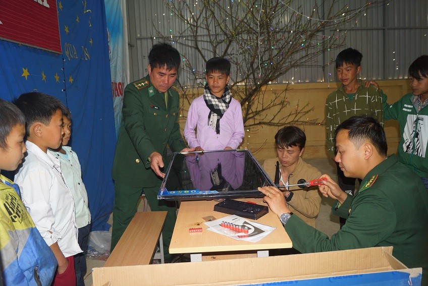 Thượng úy Phạm Tuân (ngoài cùng bên phải) đang lắp đặt chiếc tivi 40 ich mới do anh bỏ tiền túi và kêu gọi bạn bè ủng hộ dành tặng các em học sinh trường THCS Tung Qua Lìn ở huyện Phong Thổ, Lai Châu, tháng 3/2018. Ảnh: Nguyễn Minh 