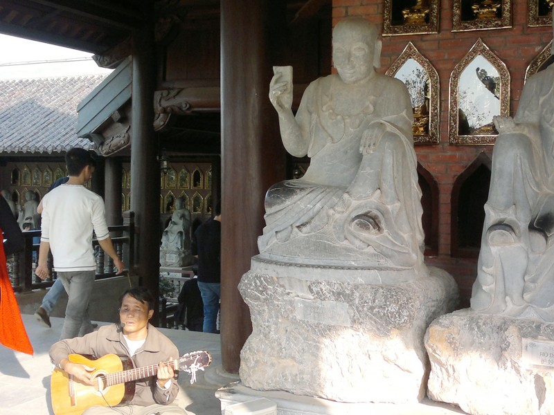 Người đàn ông mù lòa chơi bản đàn buồn bã và hát những lời ai oán về đời mình ngay cạnh những bức tượng La Hán (chụp tại chùa Bái Đính mới)