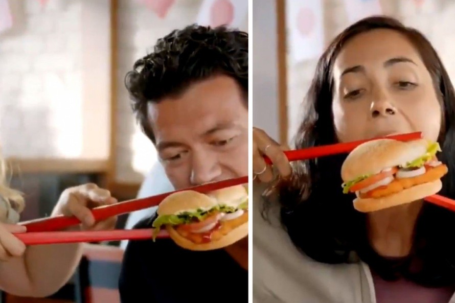 Hình ảnh nhân vật ăn bánh burger bằng đôi đũa màu đỏ cỡ lớn. (Ảnh chụp từ clip)