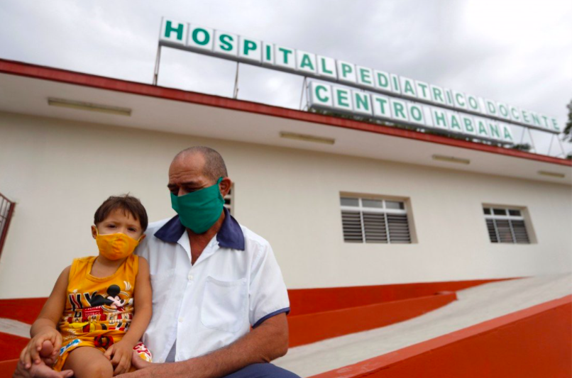 Một ông bố bế con trai bên ngoài bệnh viện ở Hanava, nơi đang triển khai tiêm vắc-xin COVID-19 cho nhóm trẻ từ 2 tuổi. (Ảnh: EPA)