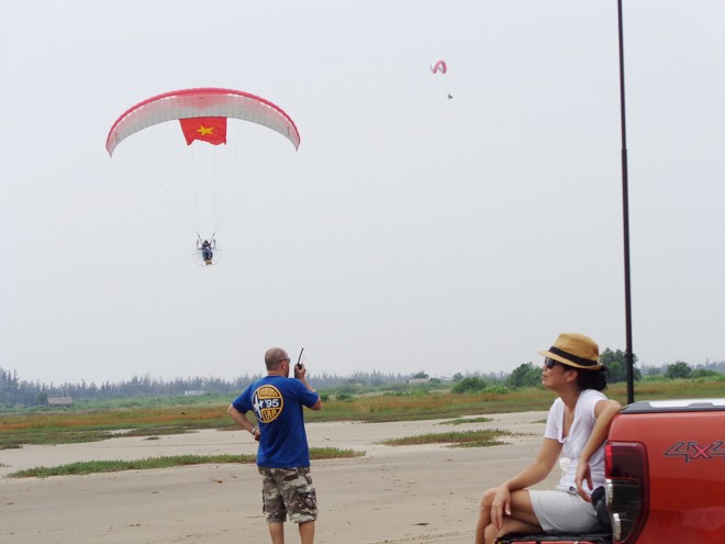 Phi công Nguyễn Tuấn Võ đang bay với lá cờ Tổ quốc. Dưới đất, anh Julien đang hướng dẫn phi công thông qua bộ đàm