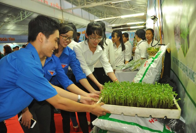 Phan Gia Thịnh (bên trái) với sản phẩm rau mầm trồng bằng đất sạch do chính anh sản xuất. Sản phẩm được trưng bày, giới thiệu tại hội chợ triển lãm nông nghiệp sạch ở Bến Tre. Ảnh: Hòa Hội.