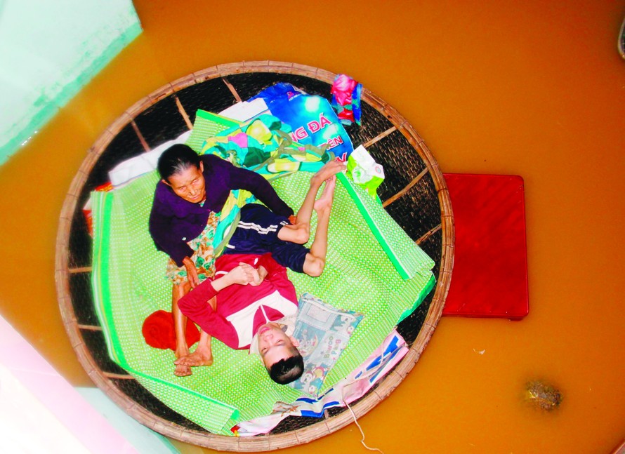 Những phận đời khốn cùng trong lũ. Trong ảnh là bà Lê Thị Đắt và con trai bị tật nguyền (thôn Tây An, xã Hòa Châu, huyện Hòa Vang, Đà Nẵng) ngồi trong thúng neo vào cột để vượt qua cơn lũ. Ảnh chụp tháng 11/2017. Ảnh: Thanh Trần