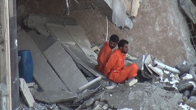 Hai tù nhân mặc áo cam bị trói ngồi bên trong ngôi nhà chờ chết