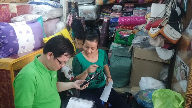 Hình ảnh nhân viên MuaBanNhanh.com hướng dẫn các tiểu thương tại chợ bán hàng bằng smartphone